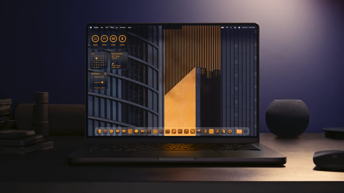A Space Black 14" MacBook Pro sitting on a desk surrounded by other black items featuring the desktop in Liquid Glass