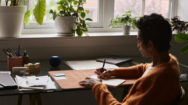 A person sitting at a desk surrounded by plants with a HomePod mini