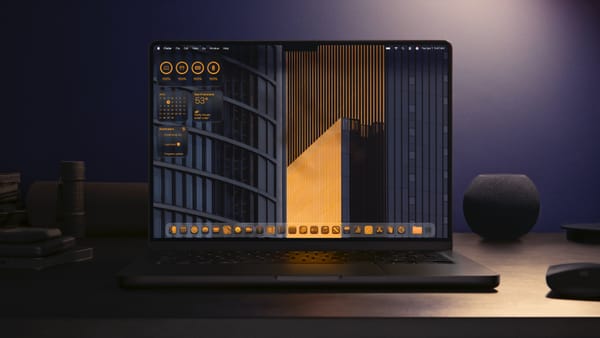 A Space Black 14" MacBook Pro sitting on a desk surrounded by other black items featuring the desktop in Liquid Glass